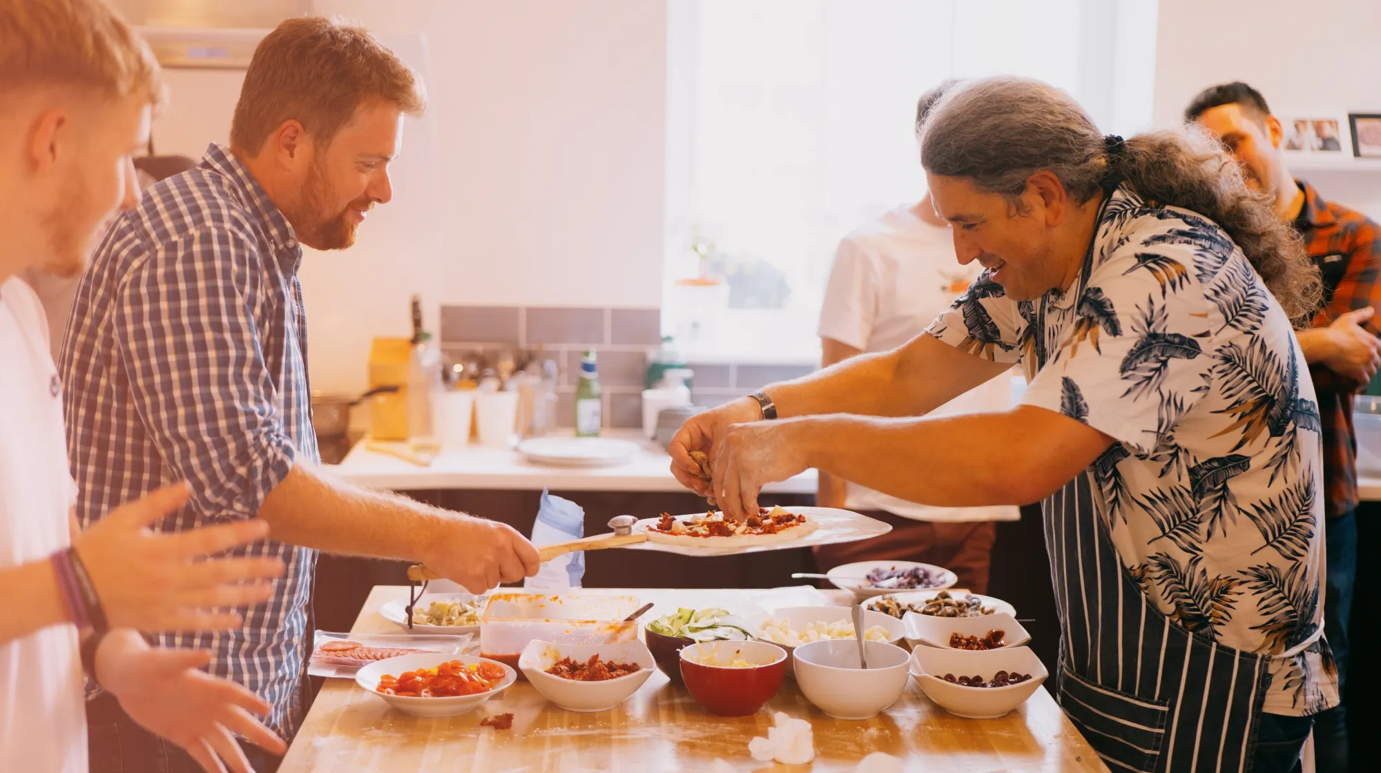 People gathered around a table making pizza.